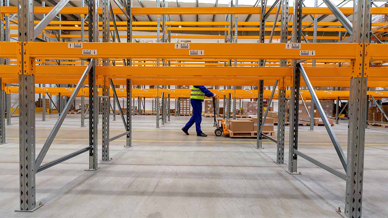 A warehouse worker pushing a pallet in the middle of empty shelves